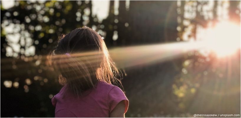 girl looks at a ray of sunshine in the forest