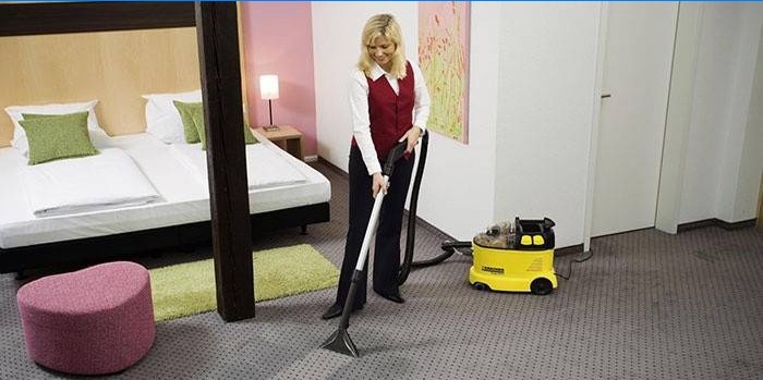 The girl is cleaning the carpet with a vacuum cleaner