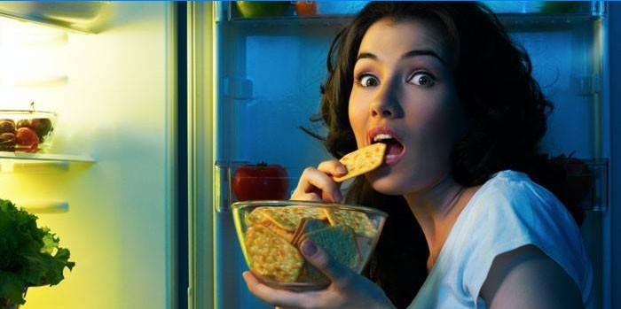 Girl in front of an open refrigerator eats crackers