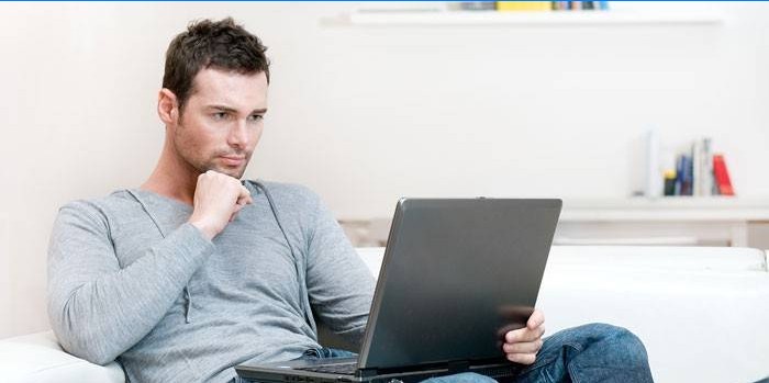 A man sits on a sofa with a laptop