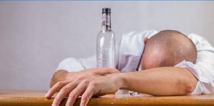 Drunk man lies on the table and holds an empty bottle in his hand