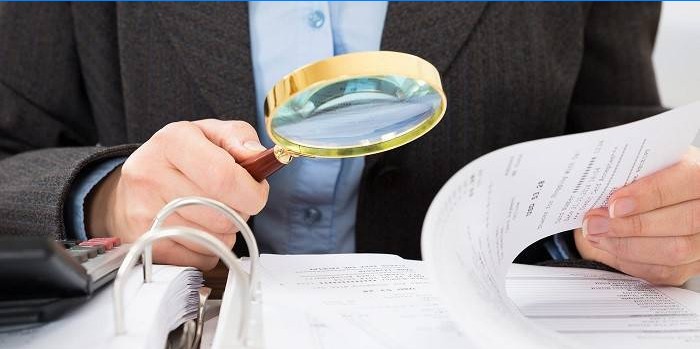 A man is studying documents with a magnifier