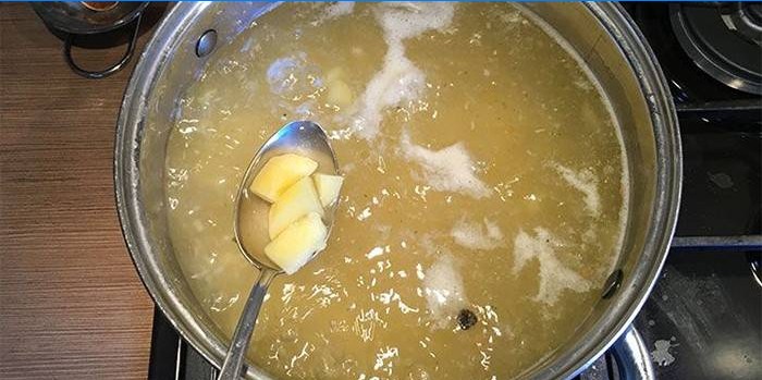 Chicken stock in a pan and potatoes in a spoon